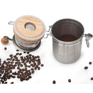 A stainless steel coffee grinder with the lid open sits in front of a white background with coffee beans scattered around it. 