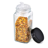 A clear glass jar filled with seasoning sits with the black cap leaning against it on a white background.