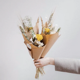 A floral bouquet wrapped in brown paper held by a hand. 
