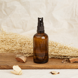 An amber spray bottle sits on a piece of wood with some straw in the background