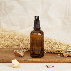 An amber spray bottle sits on a piece of wood with some straw in the background