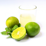 A glass filled with organic lime juice is surrounded by two whole limes and one cut lime on a white background.