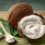 A coconut is cracked in half and filled with whipped coconut cream.  A bamboo spoon sits beside it filled with the whipped coconut.
