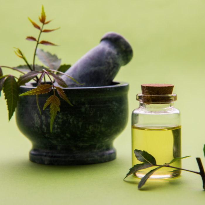 Neem oil in a small glass jar next to neem leaves in a mortar and pestle