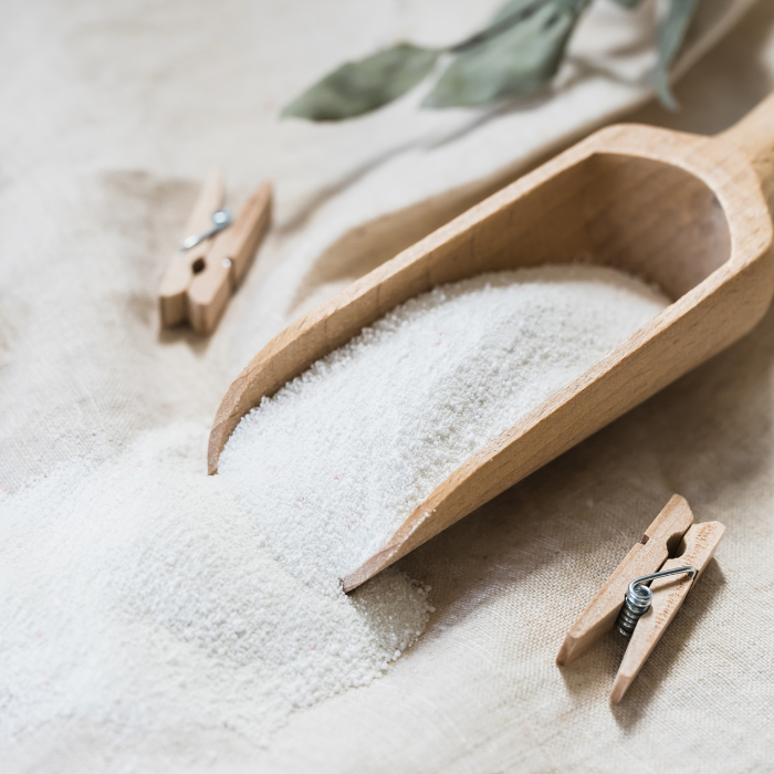 Laundry booster powder in a wooden spoon next to clothespins on a linen surface