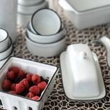 White porcelain butter dish seen in a tabletop setting with a berry basket and beautiful porcelain dish set.