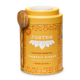 A yeallow tin of turmeric tea with a wooden scoop on the side of it sits on a white background.
